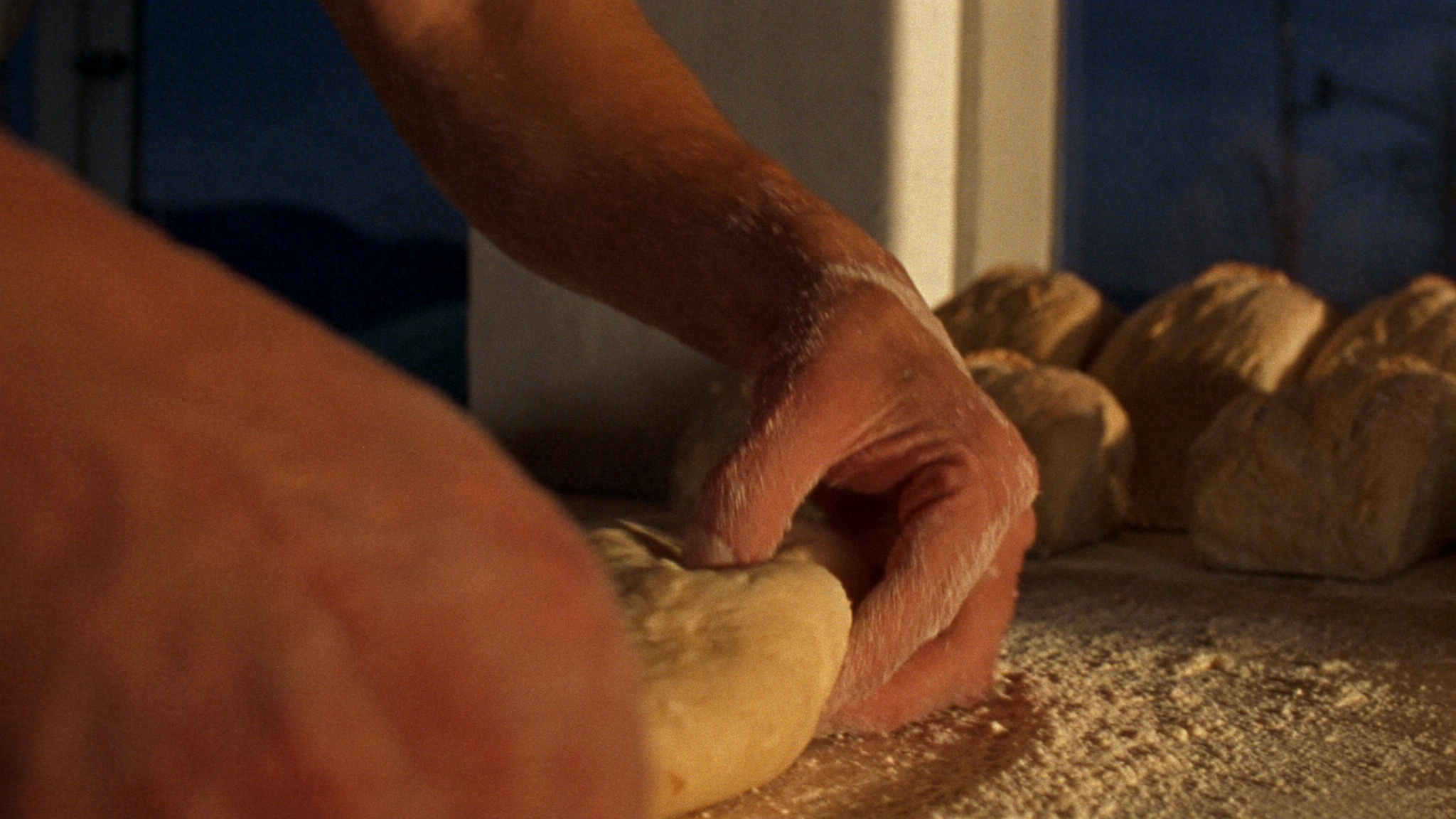 Nahaufnahme: bemehlte Hände kneten Teig auf dem Holztisch der Bäckerei Bühler